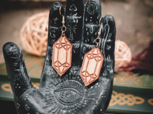 Laser cut and engraved earrings made from raw birch plywood in the shape of crystals hanging from the fingers of a hand sculpture.