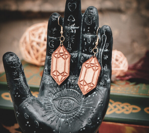 Laser cut and engraved earrings made from raw birch plywood in the shape of crystals hanging from the fingers of a hand sculpture.