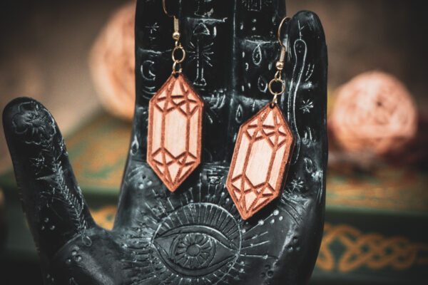 Laser cut and engraved earrings made from raw birch plywood in the shape of crystals hanging from the fingers of a hand sculpture.