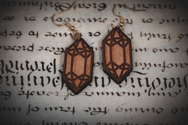 Laser cut and engraved earrings made from raw birch plywood in the shape of crystals on a sheet of calligraphy.