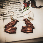 Handcrafted birch plywood raven earrings styled over an antique manuscript with medieval marginalia and whimsical drollery illustrations.