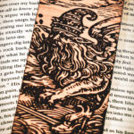 A detailed view of a handcrafted birch wood bookmark depicting a sorcerer beneath a crescent moon and stars, highlighting the intricate wood grain and dark engraved lines.