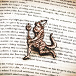 A laser engraved birch plywood pin featuring a running satyr holding a branch from the Aberdeen Bestiary on the page of an open book.