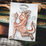A laser cut and engraved magnet made from raw birch plywood in the shape of a satyr holding a branch from the Aberdeen Bestiary in a cellophane bag with a gray card background with stylized trees leaning against a stack of books.