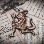 A laser cut and engraved magnet made from raw birch plywood in the shape of a satyr holding a branch from the Aberdeen Bestiary on top of various papers and a stone surface.