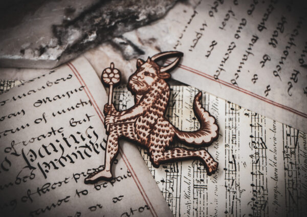 A laser cut and engraved magnet made from raw birch plywood in the shape of a satyr holding a branch from the Aberdeen Bestiary on top of various papers and a stone surface.