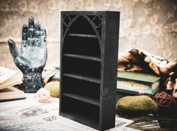 A tall, laser-cut wooden miniature bookshelf in black, featuring a prominent gothic arch and intricate quatrefoil cutouts at the top.