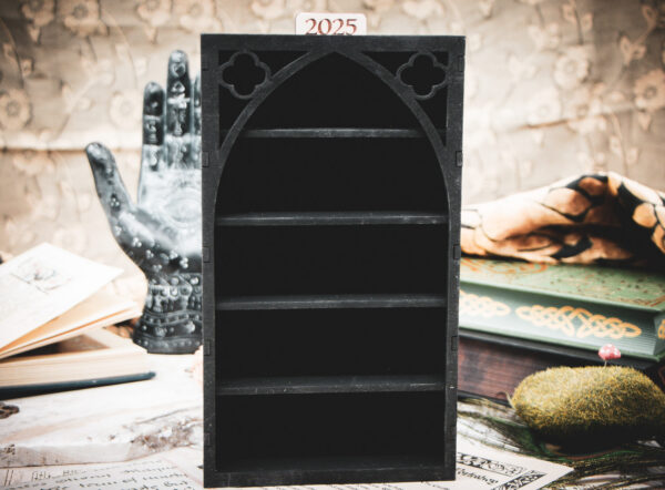 A tall, laser-cut wooden miniature bookshelf in black, featuring a prominent gothic arch and intricate quatrefoil cutouts at the top.