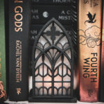 Architectural book nook lantern featuring laser-cut Gothic cathedral window tracery made from 1/8 inch birch plywood painted matte black beside books softly glowing.