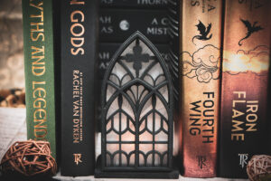 Architectural book nook lantern featuring laser-cut Gothic cathedral window tracery made from 1/8 inch birch plywood painted matte black beside books softly glowing.