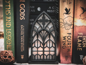 Architectural book nook lantern featuring laser-cut Gothic cathedral window tracery made from 1/8 inch birch plywood painted matte black beside books softly glowing.