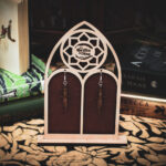 A pair of laser-cut wooden dagger earrings, the "Duelist's Shard," displayed on a cathedral-style wooden stand featuring The Griffin and Stag logo.