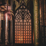 Architectural book nook lantern featuring laser-cut Gothic cathedral window tracery made from 1/8 inch birch plywood painted matte black on a bookshelf surrounded by books and gently glowing.
