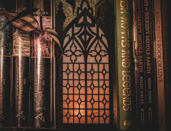 Architectural book nook lantern featuring laser-cut Gothic cathedral window tracery made from 1/8 inch birch plywood painted matte black on a bookshelf surrounded by books and gently glowing.