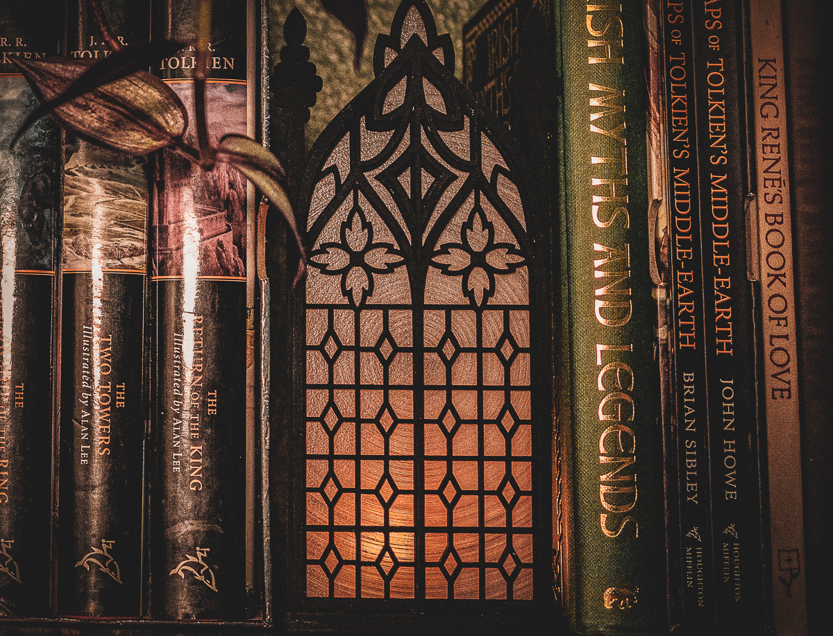 Architectural book nook lantern featuring laser-cut Gothic cathedral window tracery made from 1/8 inch birch plywood painted matte black on a bookshelf surrounded by books and gently glowing.