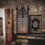 Architectural book nook lantern featuring laser-cut Gothic cathedral window tracery made from 1/8 inch birch plywood painted matte black on top of and beside books softly glowing