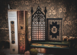Architectural book nook lantern featuring laser-cut Gothic cathedral window tracery made from 1/8 inch birch plywood painted matte black on top of and beside books softly glowing