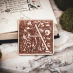 Square birch wood magnet featuring Hans Holbein the Younger's Danse Macabre alphabet letter A woodcut from 1523.