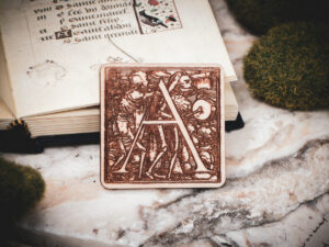 Square birch wood magnet featuring Hans Holbein the Younger's Danse Macabre alphabet letter A woodcut from 1523.