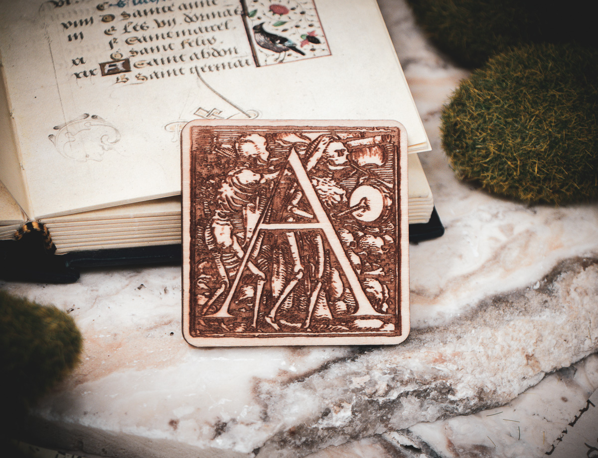 Square birch wood magnet featuring Hans Holbein the Younger's Danse Macabre alphabet letter A woodcut from 1523.