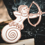 A close-up of the Slow-Shot Sentinel magnet made of laser cut and engraved raw birch plywood in the shape of a man with a snail shell for legs aiming a bow and arrow.