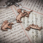 A close-up of three of a set of six laser cut and engraved birch magnets featuring rabbits waging battle against knights in a castle tower on top of various papers and a stone surface.