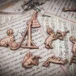 A close-up of four of a set of six laser cut and engraved birch magnets featuring rabbits waging battle against knights in a castle tower on top of various papers and a stone surface.