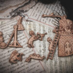 A set of six laser cut and engraved birch magnets featuring rabbits waging battle against knights in a castle tower on top of various papers and a stone surface.