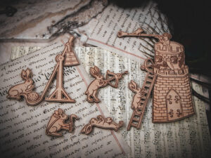 A set of six laser cut and engraved birch magnets featuring rabbits waging battle against knights in a castle tower on top of various papers and a stone surface.