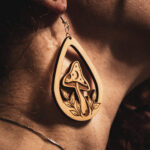 A close-up side profile of a person wearing a Mycelial Mystic earring, showcasing the detailed engraving and natural wood grain against a warm, sunlit background.