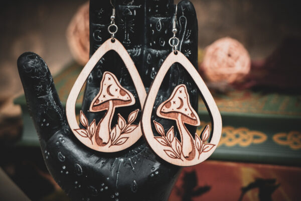 The teardrop mushroom earrings styled on a black, ornate palmistry hand model, surrounded by dark academia-themed decor and vintage books.