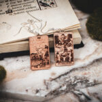 Laser cut and engraved earrings made with 1/16" birch plywood featuring the images of the Tarot cards "The Star" and "Judgement" leaning against an open illuminated manuscript surrounded by moss rocks on a slab of stone.