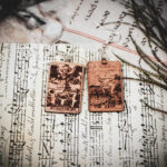 Laser cut and engraved earrings made with 1/16" birch plywood featuring the images of the Tarot cards "Judgement" and "The Star" on top of papers and a peacock feather on a stone surface.