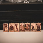 Laser cut and engraved earrings made with 1/16" birch plywood featuring the images of the Major Arcana of the Tarot lined up leaning against paperback books with black page edges.
