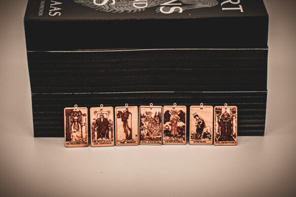 Laser cut and engraved earrings made with 1/16" birch plywood featuring the images of the Major Arcana of the Tarot lined up leaning against paperback books with black page edges.