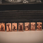 Laser cut and engraved earrings made with 1/16" birch plywood featuring the images of the Major Arcana of the Tarot lined up leaning against paperback books with black page edges.