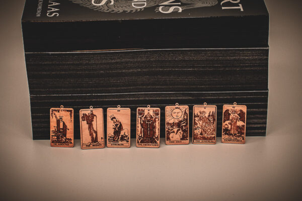 Laser cut and engraved earrings made with 1/16" birch plywood featuring the images of the Major Arcana of the Tarot lined up leaning against paperback books with black page edges.