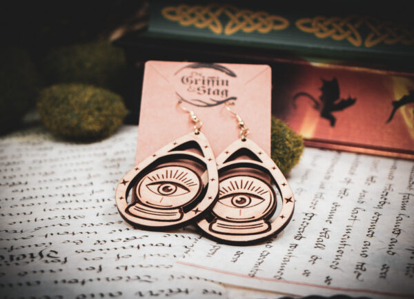 Handcrafted crystal ball earrings displayed on a "The Griffin and Stag" backing card atop pages of hand written calligraphy in a dark academia setting.