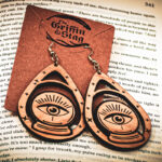 Handcrafted crystal ball earrings displayed on a "The Griffin and Stag" backing card atop the page of a fantasy hardcover book.