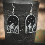 The silver-engraved mountain earrings hanging from the rim of a dark, ornate metal chalice.