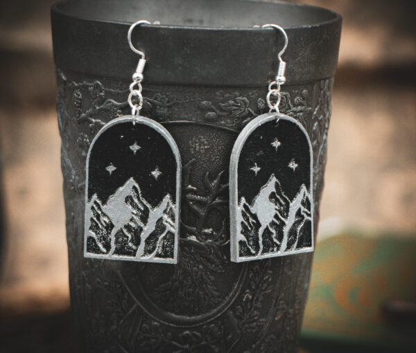 The silver-engraved mountain earrings hanging from the rim of a dark, ornate metal chalice.