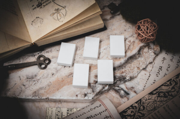 A set of 5 3D printed miniature book blanks arranged on a piece of stone surrounded by books, and papers