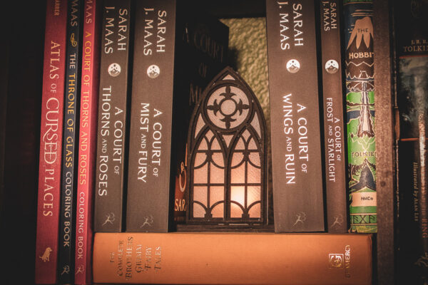 Architectural book nook lantern featuring laser-cut Gothic cathedral window tracery made from 1/8 inch birch plywood painted matte black on top of and beside books softly glowing.